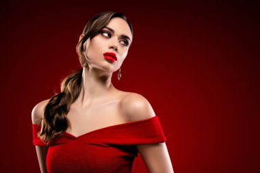 Kırmızı şık bir elbise giymiş güzel bir genç bayan göz alıcı makyaj ve takılarla şık görünüyor. Sofistike bir ifade, cesur bir kırmızı arka plana karşı güven, lüks ve çekicilik taşır..