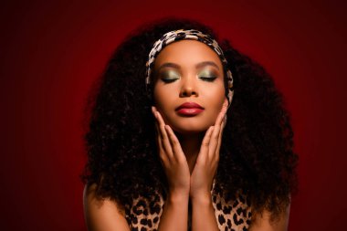 Zarif makyajı, kıvırcık saç stili ve leopar desenli modası olan şık bir kadın, özgüvenle poz veriyor, koyu kırmızı bir arka plan, lüks, zarafet ve cazibeye bürünüyor.