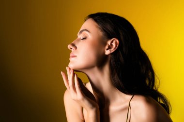 Zarif bir esmer canlı sarı bir arka plana karşı sakin bir profille poz veriyor, sofistike ve zarafet yayıyor, zarafetin ve modern güzelliğin özünü somutlaştırıyor.