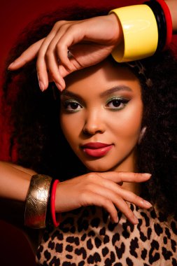 Göz alıcı makyajı, bilezikleri, leopar desenli elbisesi ve canlı kırmızı stüdyosunda tropikal temalı aksesuarları olan güzel bir kadın..