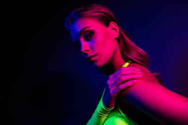 Genç kadın neon ışığın altında poz veriyor, canlı renkli ve modaya uygun bir atmosfer yaratıyor. Güzellik, tarz ve modern trendler için mükemmel.