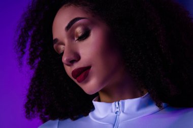 Cüretkar makyajlı, kıvırcık saçlı parlak mor neon ışıklarla aydınlatılmış zarif, tarz ve modern güzellikle çarpıcı bir kadın görüntüsü..