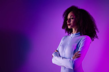 Model, modern güzelliği, zarafeti ve modaya uygun estetiği, canlı renkleri ve çağdaş tasarımı örnek alan, şık mor ışığın ortasındaki pohpohlayıcı kıyafetlerle güven verici bir şekilde poz verir..