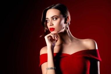 Kırmızı omuzlu bir elbise giyen, zarif mücevherler sergileyen ve cesur ve çarpıcı bir arka plana karşı özgüven saçan çekici bir kadın manken..