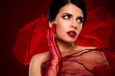 Zarif bir kadın model göz alıcı ve lüks bir görünüm sergiliyor canlı kırmızı kumaşla mistik ve büyüleyici bir atmosfer yaratıyor. Güzellik, zarafet ve yüksek moda içeren temalar için mükemmel..
