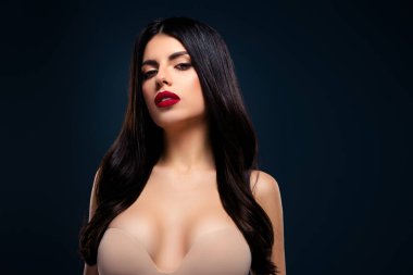 Göz kamaştırıcı makyajlı, koyu renk saçlı ve koyu kırmızı rujlu karamsar mavi arka planda, ışıl ışıl bir tarzı, kendine güveni ve kadınsı cazibesi olan çarpıcı bir genç kadın..