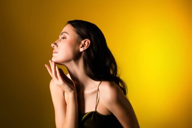 Şık giyinmiş genç bir esmer kadın zarif bir şekilde canlı sarı bir arkaplanda poz veriyor, sanatsal ve büyüleyici bir kompozisyonda doğal güzelliğini ve şıklığını vurguluyor..