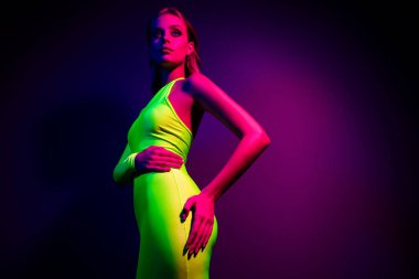 Canlı, yeşil bir elbise içinde, ultraviyole ışık altında şık genç bir kadın, çağdaş sanat estetiği ve büyüleyici titreşimleriyle şık bir kulüp atmosferi yaratıyor..