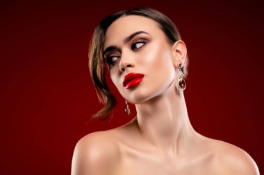 Kusursuz makyajlı ve zarif küpeleri olan göz kamaştırıcı bir kadın, koyu kırmızı bir arka planla işaretlenmiş. Lüks, zarafet, kutlama, güzellik ve yüksek moda temaları için ideal.