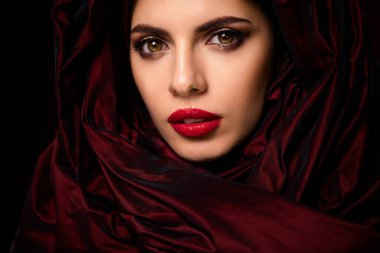 Göz alıcı makyajı ve şık modası olan, zarif, şehvetli ve lüks bir genç bayanın yakın çekimi, kırmızı ve göz kamaştırıcı koyu bir arka planı var..