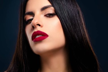 Göz alıcı kırmızı ruju, göz alıcı makyajı ve kendine güvenen koyu renk saçı olan şık bir kadının yakın plan görüntüsü. Samimi çekim, sofistike bir atmosferdeki güzelliği ve cazibeyi ön plana çıkarıyor..
