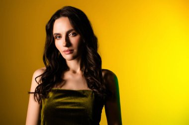 Zarif bir elbise içinde genç esmer bir kadının portresi, parlak sarı bir arkaplanda poz veriyor, modern güzellik ve tarzın vücut bulmuş hali..