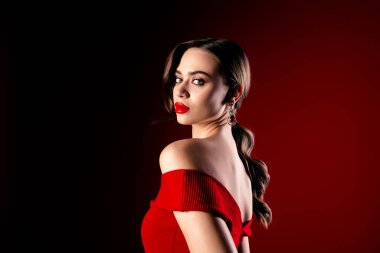 Göz alıcı kırmızı bir elbise giymiş ışıl ışıl mücevherlerle süslenmiş şık bir esmer lüks temalı, loş bir arka plana karşı kendine güven ve zarafet saçıyor..