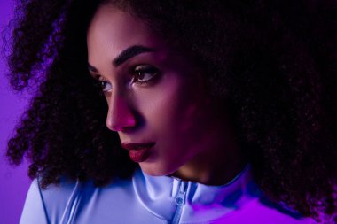 Büyüleyici bir genç kadın neon ışıklı bir ortamda, şık giyinmiş, kusursuz makyajlı, canlı ve modaya uygun mor bir arka planda modern güzellik ve zarafet yayıyor..