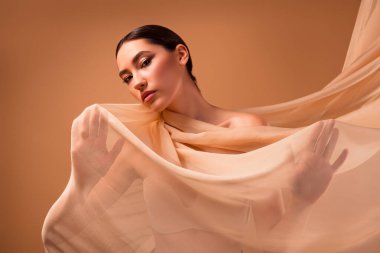 Güzel esmer bir kadının portresi bej kumaşla kaplanmış, entellektüellik, zarafet ve moda zarafeti sergiliyor..