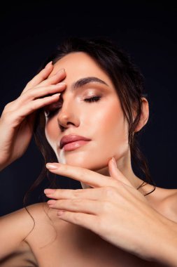 Zarif makyajlı, zarif saçlı, kusursuz cildine odaklanmış esmer bir kadının portresi ve koyu bir arkaplan karşısında çekici bir ifade..