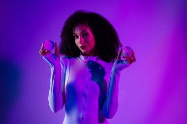 Şık, genç bir kadın, kendine güvenen bir vücut giysisiyle poz veriyor, dinamik neon ışıkla aydınlatılıyor, modern güzellik ve moda sergiliyor. Lüks ve cazibeyi vurgulayan kozmetik konteynırlar taşıyor..