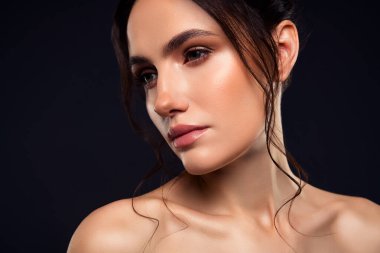 Pürüzsüz, esmer saçlı, parlak tenli, zarif ve doğal güzelliği ifade eden güzel bir kadın, koyu, minimalist bir zemin üzerine kurulmuş.