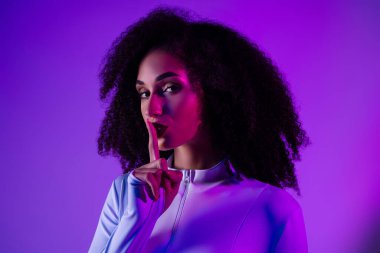 Kendine güvenen genç bir kadın canlı mor bir poz veriyor ve parlak bir arka planda beyaz şık bir elbise giyiyor..