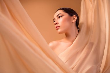 Saf kumaşı kucaklayan zarif bir esmer poz. Güzelliği, cilt bakımını ve moda anlayışını ön plana çıkarıyor..