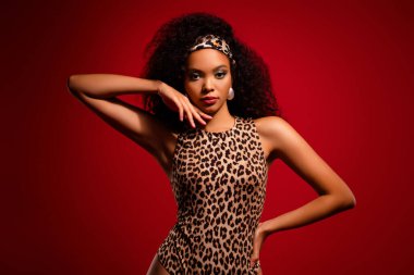 Leopar desenli kıyafet ve klasik saç bandı giyen zarif bir genç kadın. Kalın kırmızı arka plan, onun güzelliğini, stilini ve şık görünümünü vurguluyor..