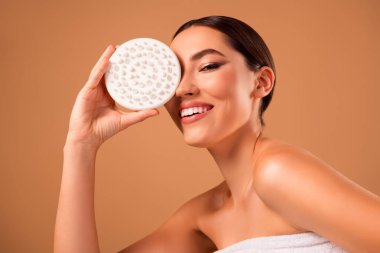 Güzel, genç, esmer bir kadın, elinde bir vücut masajı fırçasıyla arka planda çıplak bir şekilde gülümsüyor. Cilt rutini, güzellik, kendini sevme, kişisel bakım ve parlayan sağlıklı cilt kavramları..