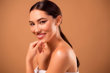 Şık, esmer saçlı, kusursuz tenli, yumuşak bej bir arka planı olan zarif bir kadının portresi göz alıcı ve şık bir stüdyo ortamında güzelliği ve cildi kucaklıyor..