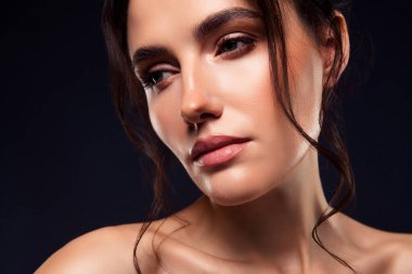 Temiz cildini, doğal makyajını ve sofistike saç stilini sergileyen esmer bir kadının göz kamaştırıcı yakın çekimi. Karanlık bir arkaplanda, zarafet ve güzelliği yansıtıyor..