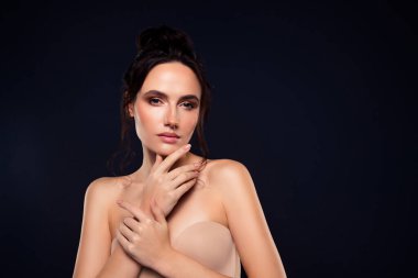 Sağlıklı, parlak tenli, genç ve çekici bir kadın, koyu bir arka plan karşısında zarifçe poz veriyor, özgüven ve sadelik gösteriyor..