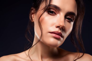 Profesyonel makyajlı, stil sahibi, ışık saçan güzel ve sofistike bir kadın. Göz kamaştırıcı bir efekt için karanlık bir arkaplanda yakalanmış..