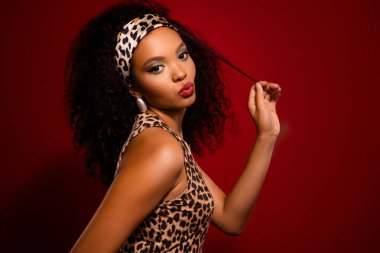 Çekici bir genç kadın, kırmızı arka planda zarif poz veriyor, leopar desenli bir kıyafet giyiyor ve bukleleri var. Güzelliği, cazibeyi, modayı ve zarafeti temsil eder..