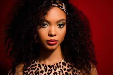 Çarpıcı bir şekilde stil sahibi bir kadın kırmızı arka planda poz veriyor, leopar desenli elbisesini, doğal kıvırcık saçlarını ve kalın makyajını gösteriyor..