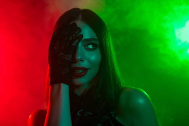 Gizemli bir kadın dramatik bir şekilde poz veriyor. Renkli kırmızı ve yeşil karamsar renklerle çevrili. Cadılar Bayramı teması için mükemmel..