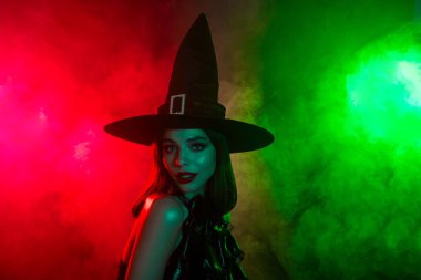 Çarpıcı kırmızı ve yeşil ışık altında poz veren büyüleyici cadı, sonbahar tatili görselleri, mistik temalar ve büyüleyici kavramlar için ideal.
