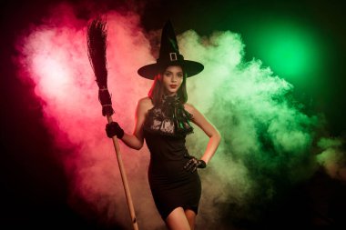 Cadı kostümlü bir kadın sisli bir ortamda poz veriyor, canlı kırmızı ve yeşil ışıklar, Cadılar Bayramı 'nın büyülü ruhunu çağrıştırıyor..