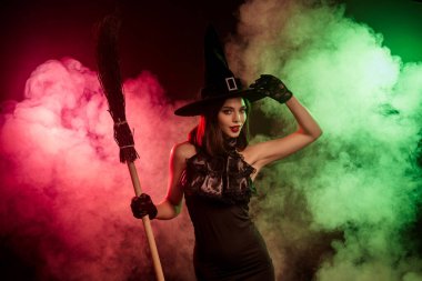 Büyüleyici mistik sahne, elinde süpürge sopası olan şık bir cadının canlı renkli dumanla çevrili, Cadılar Bayramı 'nı, büyüyü ve büyüyü simgeleyen.