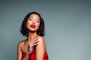 Stylish brunette woman against a grey background, showcasing confidence and elegance through her glamorous appearance, chic fashion, and mesmerizing makeup.