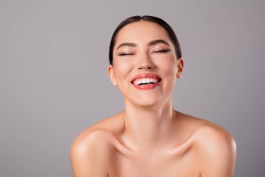 Charming young woman showcasing flawless skin and a radiant smile, emphasizing her confident and natural beauty, complemented by a grey backdrop.