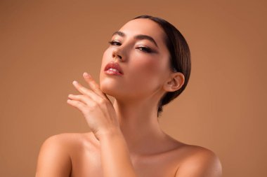 A stylish and graceful young lady posing against a harmonious beige backdrop, showcasing flawless makeup, glowing skin, and a captivating elegance.