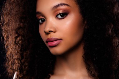 Close-up portrait of a young woman with curly hair and perfect makeup, expressing beauty, style, and elegance in a glamorous setting.