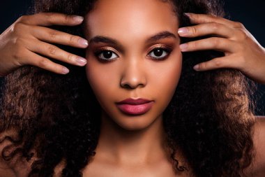A close-up studio portrait of a young woman with curly hair and perfect natural makeup, emphasizing skin health and beauty.