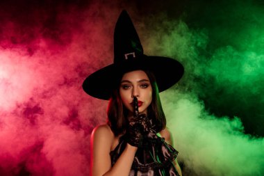 A spellbinding woman dressed as a witch, wearing a black pointed hat and surrounded by vivid green and red fog, evokes Halloween mystique.