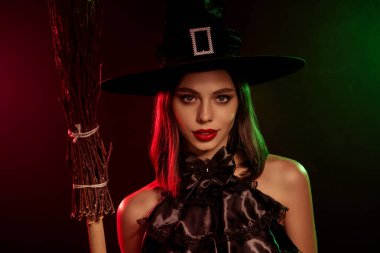 A captivating female witch in a black hat holds a broom, evoking a trendy magical Halloween vibe accented by enchanting and modern elements.