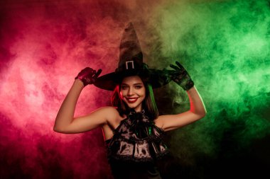 A stylish woman dressed as a witch in a dark costume, surrounded by vibrant colorful mist, ideal for magical and Halloween-themed designs.