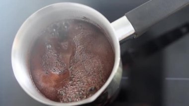 Aromatik kahve Türk 'te kaynıyor ve köpükler ağzına kadar doluyor. Sabah kahvaltısı ya da kahve molası için bir içki. Bir kafede ya da mutfakta sıcak bir içecek hazırlamanın geleneksel yolu. Yavaş çekim.