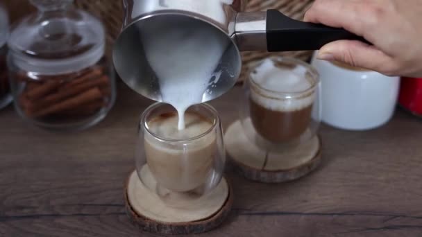 女性の手は ガラスカップの中で新鮮なコーヒーにタークから泡でミルクを注ぎます 朝食コーヒーのコンセプト 自宅でコーヒーを作るプロセス スローモーション — ストック動画