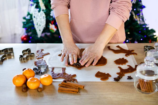 A woman makes gingerbread at home in the background of a Christmas tree. Christmas decoration in the kitchen. Fir tree with fairy lights. The concept of the New Year and Christmas.