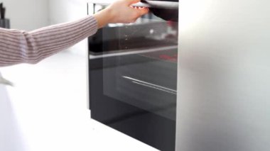 Kadınlar fırını açarlar ve fırından bir çarşaf çıkarırlar. Beyaz, modern bir mutfakta fırında yemek pişiren genç bir kadın. Noel ve Yeni Yıl kavramı.