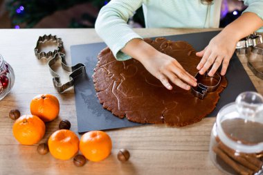 Mutlu küçük kız evde zencefilli ekmek yapıyor. Mutfakta Noel süsü var. Peri ışıklarıyla fidan ağacı. Yeni yıl ve Noel konsepti.