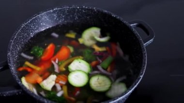 Vegetables are boiled in a casserole. Vegetables spin around in a pot with hot water. Slow-motion. The concept of vegetarianism and healthy organic food.